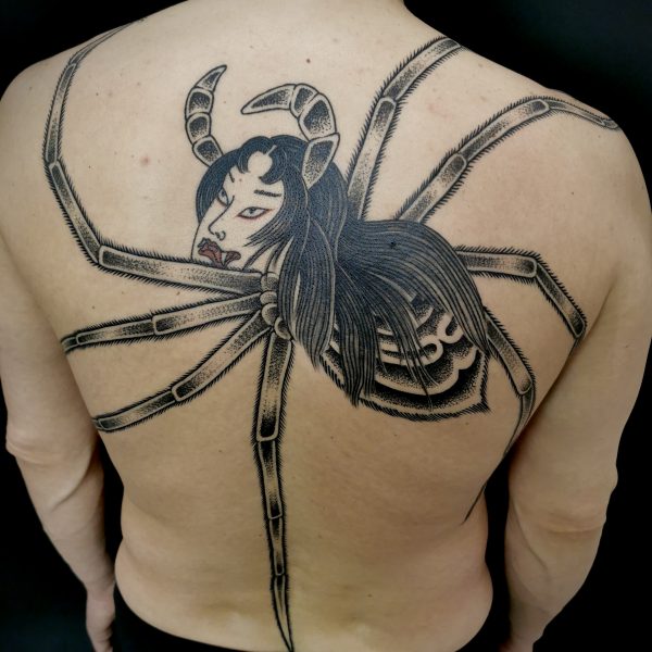 A man's back tattooed with the image of a large female spider Yokai. The tattoo pays homage to the cult Japanese film, Irezumi and was applied by Antony Dickinson at Nowhere Tattooing in Brighton UK
