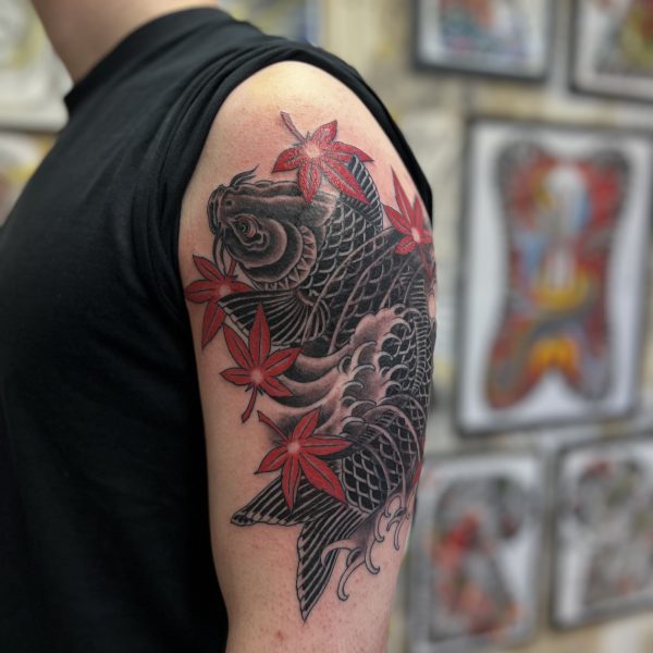 Inspired by traditional Japanese woodblock, pictured is a custom tattoo design featuring a koi and red maple leaves, momiji. The koi is in black and grey with crashing waves. The koi swimming upwards represents resilience, perseverance, and determination in the face of adversity and was completed by Tattoo Artist, Antony Dickinson. Based in London and Brighton, West Sussex at Nowhere Tattoo and Gallery